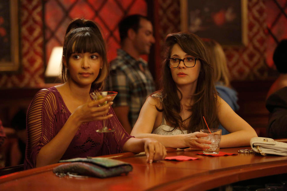 Two women sit at a bar, one holding a martini and the other with a drink