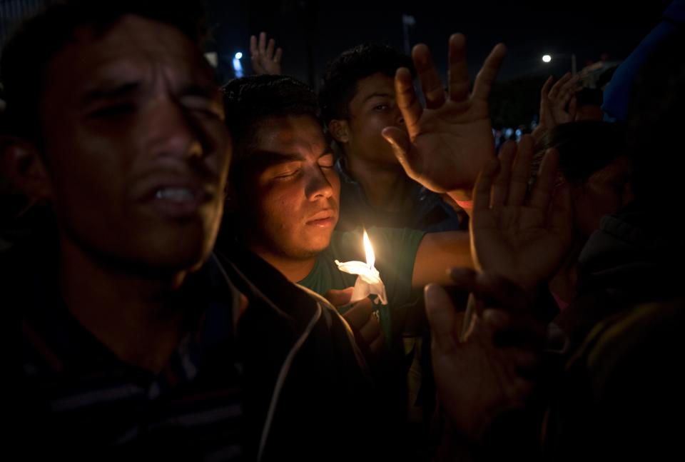 Migrants pray during a vigil outside the Benito Juarez Sports Center serving as a temporary shelter for Central American migrants in Tijuana, Mexico, Saturday, Nov. 24, 2018. The mayor of Tijuana has declared a humanitarian crisis in his border city and says that he has asked the United Nations for aid to deal with the approximately 5,000 Central American migrants who have arrived in the city. (AP Photo/Ramon Espinosa)