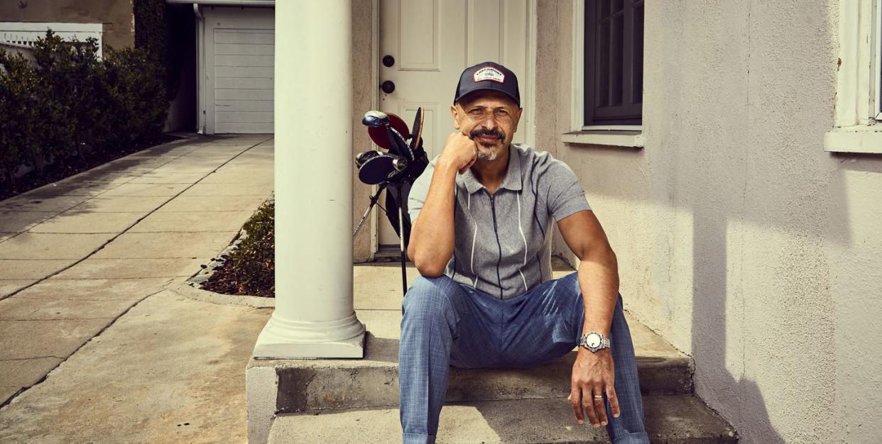maz jobrani sitting on a step with golf clubs in backgrouns