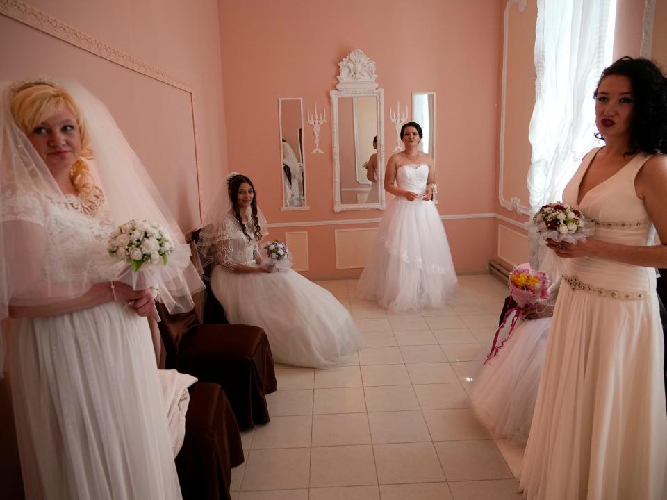 Four women in wedding dresses pose for a photo.