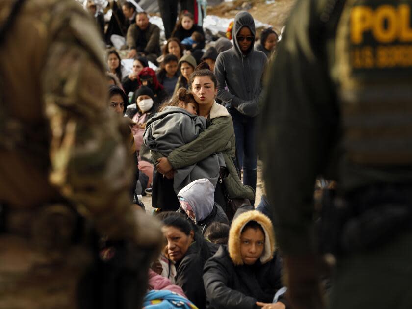 Migrants wait next to Border Patrol agents.