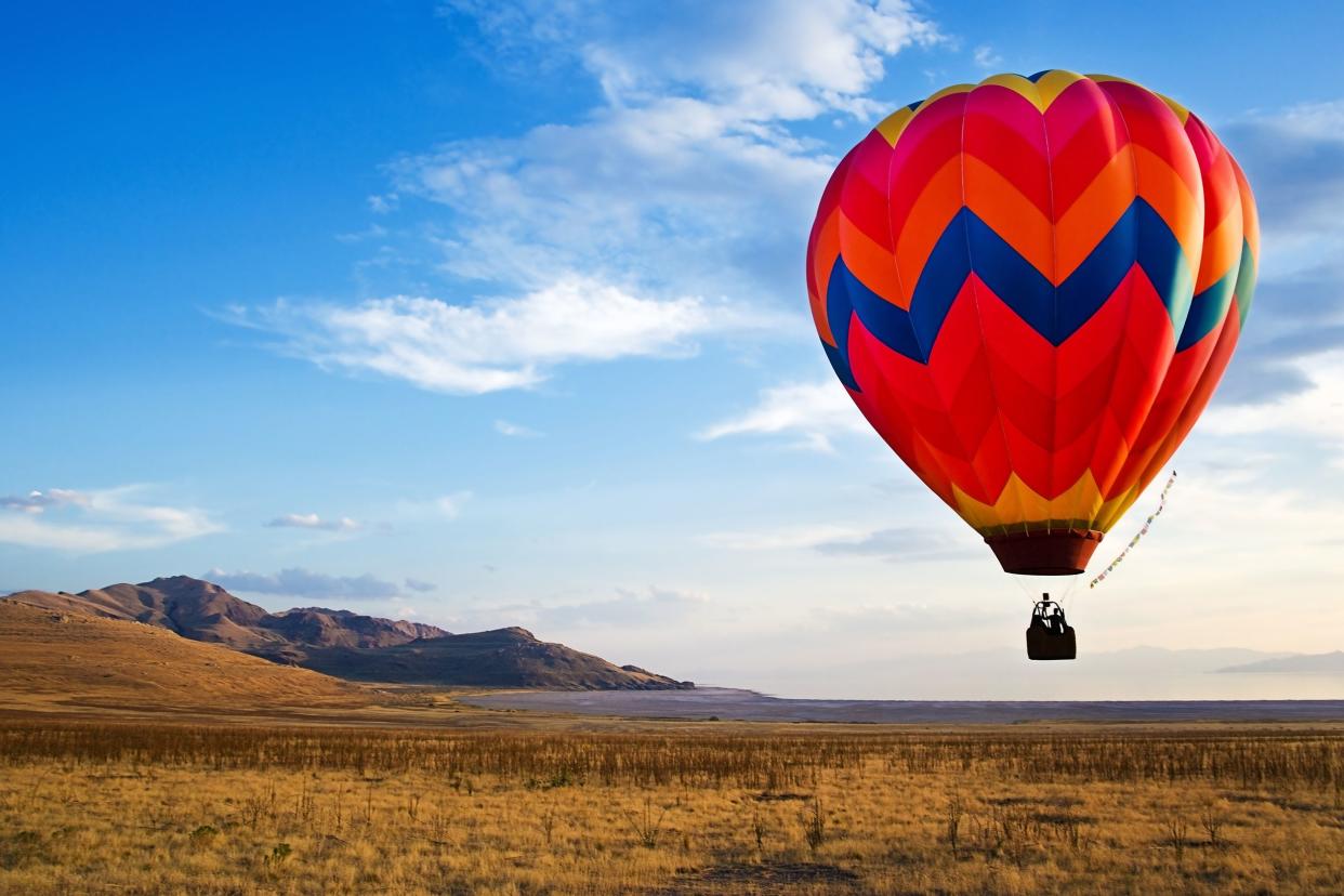Red, blue and yellow hot air balloon over flat land with hills in background