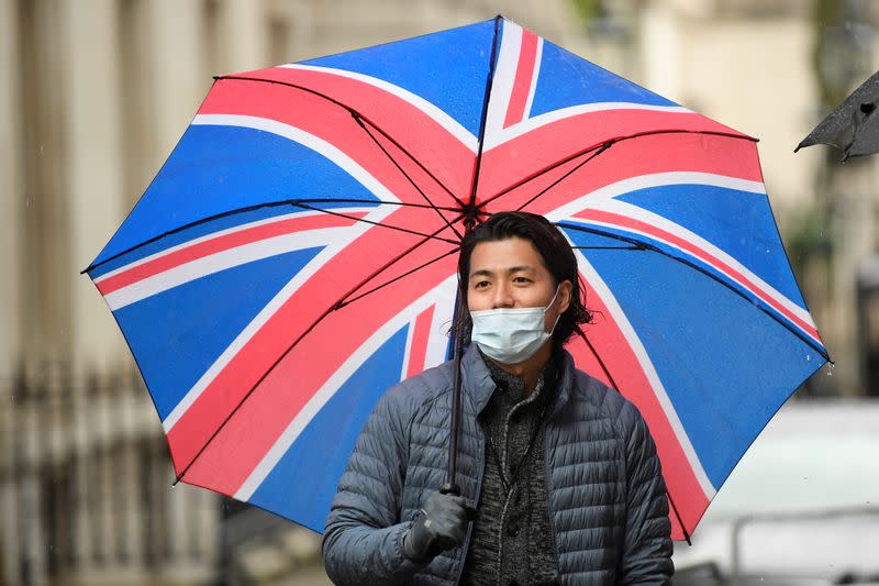 Un miembro de la prensa usa una mascarilla y sostiene una sombrilla mientras espera afuera del número 10 de Downing Street, luego del brote del COVID-19, la enfermedad causada por el coronavirus, en Londres