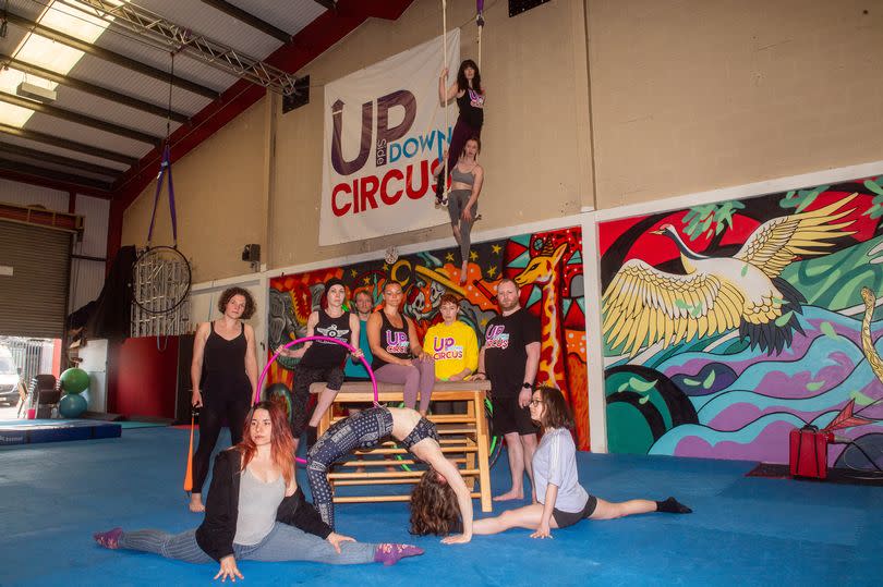 Members of the circus group in varying circus poses on a piece of equipment in the middle of a large gymnasium