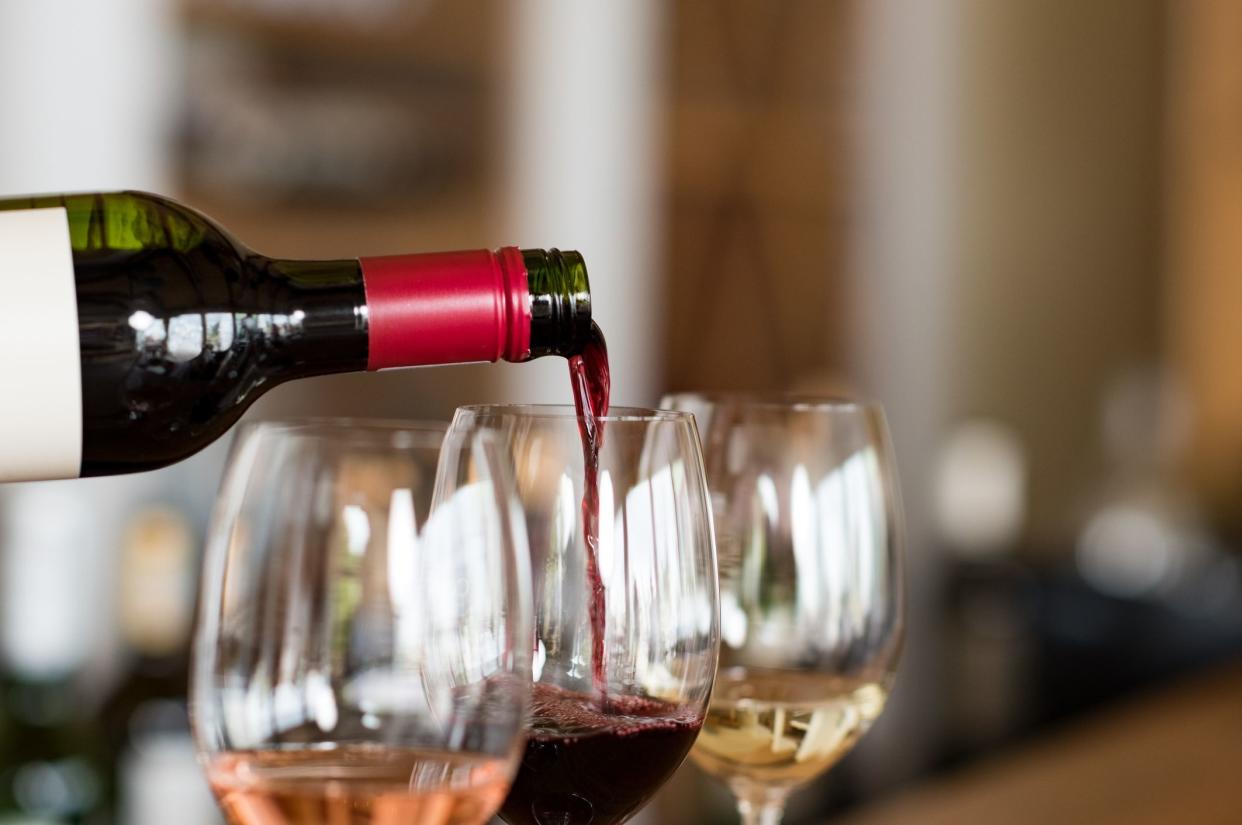 Pouring red wine from bottle into the wineglass on bar. Close up of red wine pouring from bottle to glass in a winery. Wine tasting in a winehouse.