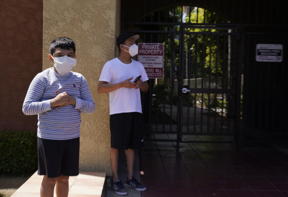 Francisco, 9, stands outdoors with his father Francisco Navas, as Los Angeles Police investigate the scene of a crime across their apartment complex in Reseda, Calif., Saturday, April 10, 2021. A woman discovered her three grandchildren, all under the age of 5, slain inside a Los Angeles apartment Saturday morning and their mother gone, police said. The mother of three children — all under the age of 5 — found slain inside a Los Angeles apartment Saturday morning has been arrested, police said. (AP Photo/Damian Dovarganes)