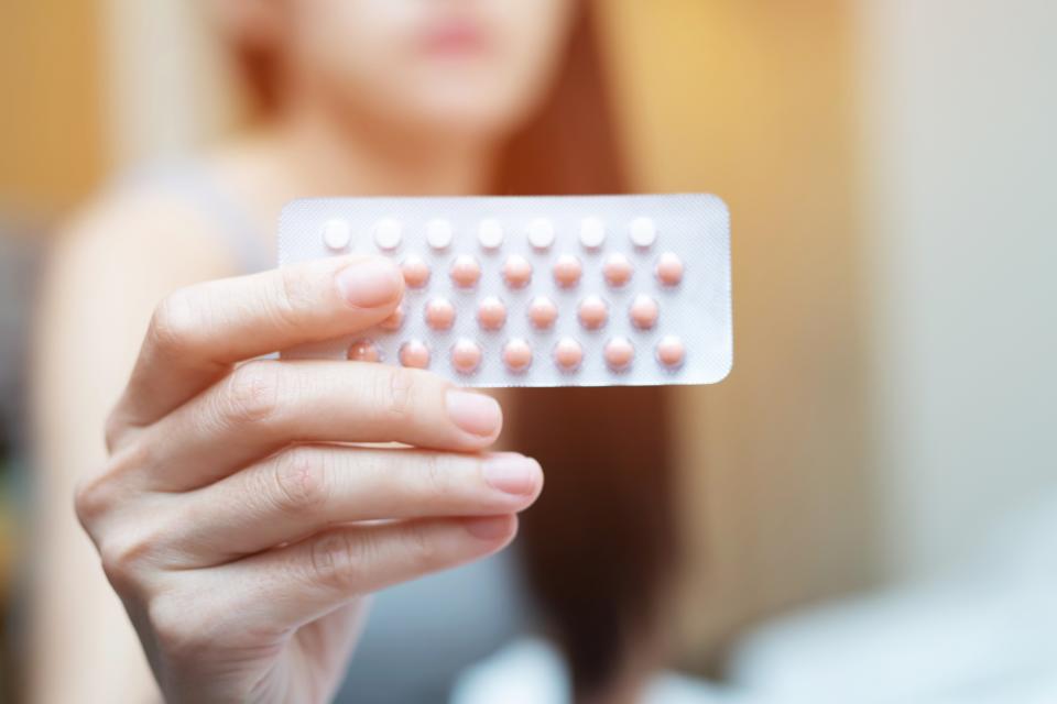 Woman hands opening birth control pills in hand on the bed in the bedroom. Eating Contraceptive Pill.