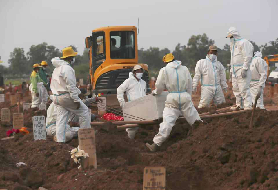 Workers in protective gear lower a coffin of a COVID-19 victim for burial at the special section of the Pedurenan cemetery in Bekasi, West Java, Indonesia, Friday, July 30, 2021. Indonesia surpassed the grim milestone of 100,000 official COVID-19 deaths on Wednesday, Aug. 4, 2021, as the country struggles with its worst pandemic year fueled by the delta variant, with growing concerns that the actual figure could be much higher with people also dying at home. (AP Photo/Achmad Ibrahim)