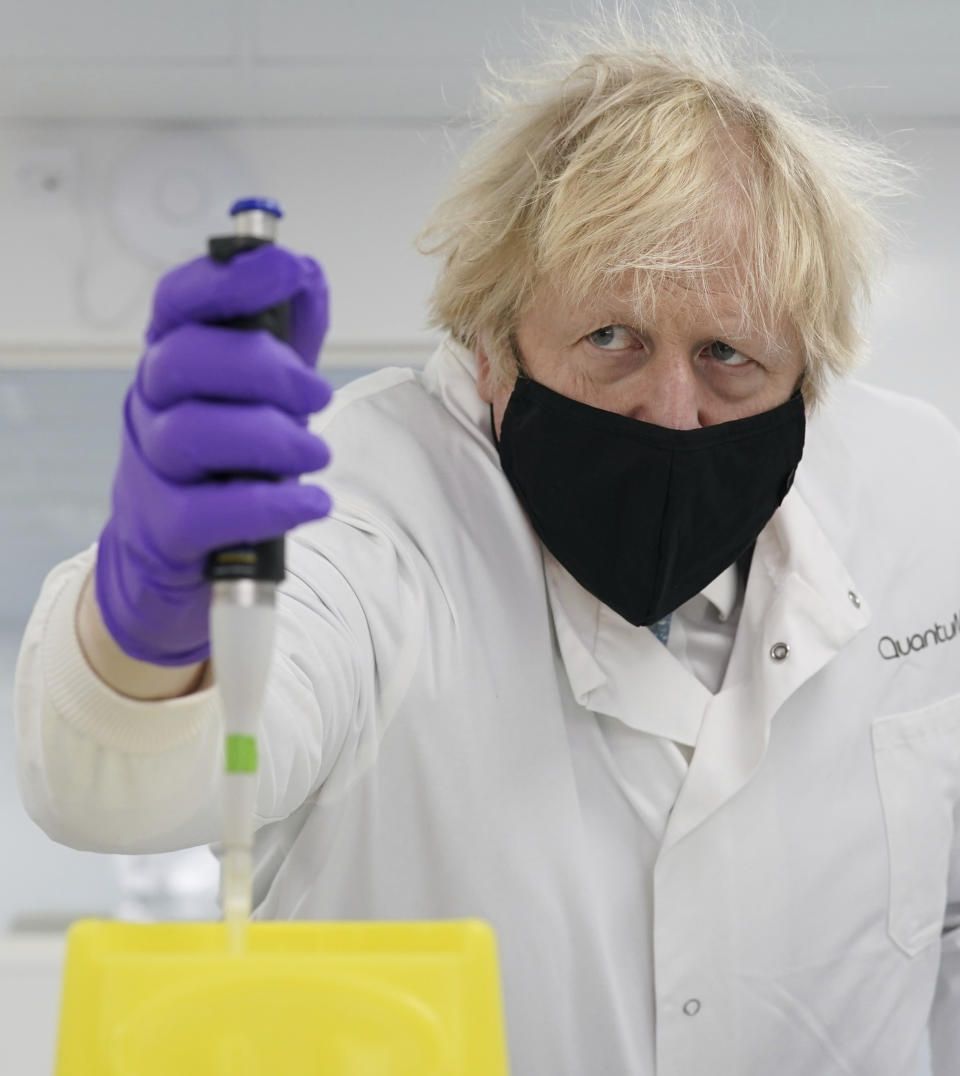 Britain's Prime Minister Boris Johnson looks at a pipette before him, during briefing by a molecular biologist at the QuantuMDx Biotechnology company in Newcastle, England on Saturday Feb.13, 2021. Johnson is visiting manufacturing facilities in north east England to see ongoing Covid-19 responses in the region. (Ian Forsyth/Pool via AP)