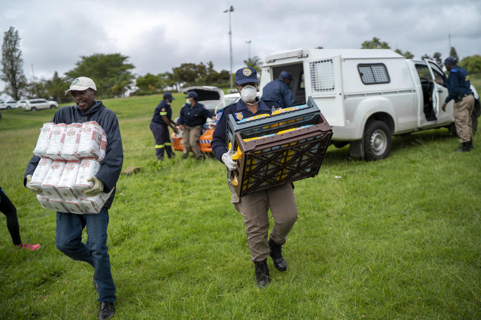 South African police help distribute food to homeless recyclers and other destitute people, some of whom said they have not eaten in three days practice social distancing as they lineup in a Johannesburg park, waiting to receive food baskets from private donors, Thursday, April 9, 2020. Because of South Africa's imposed lockdown to contain the spread of COVID-19, many people who don't have savings and are unable to work are not able to buy food.(AP Photo/Jerome Delay)