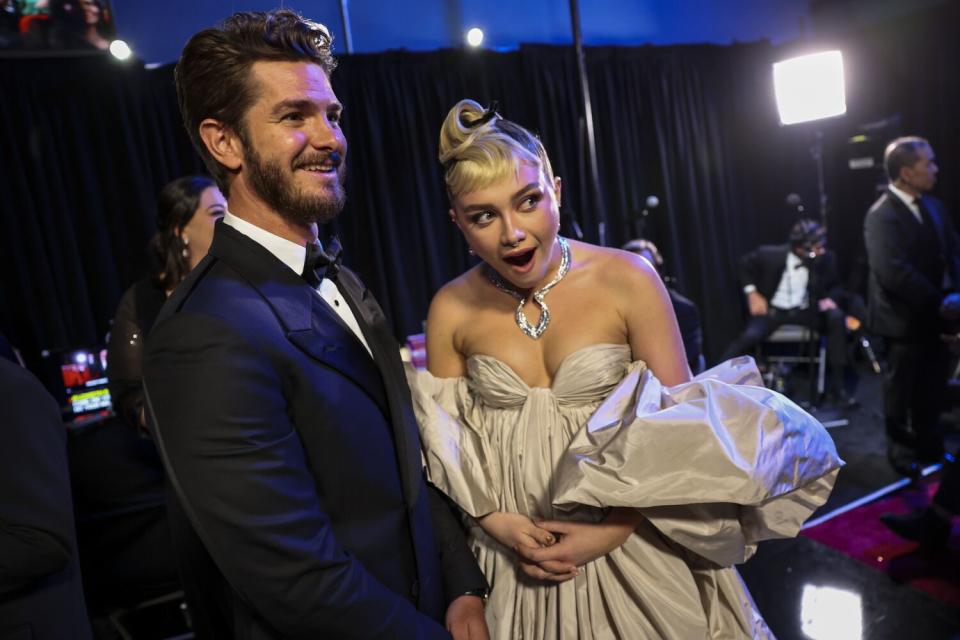 A smiling man in a tux and a surprised-looking woman in a champagne-colored dress backstage at the Oscars.