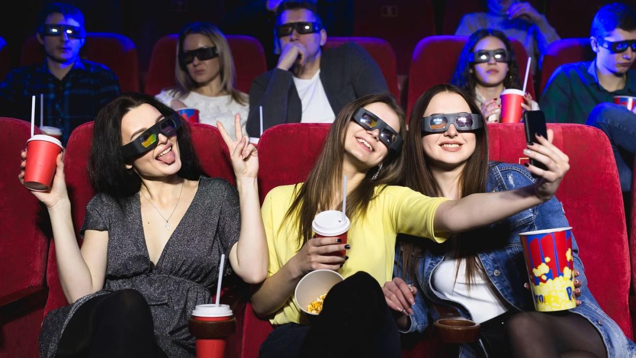 three beautiful female friends laughing happily making a selfie together during a movie at the cinema