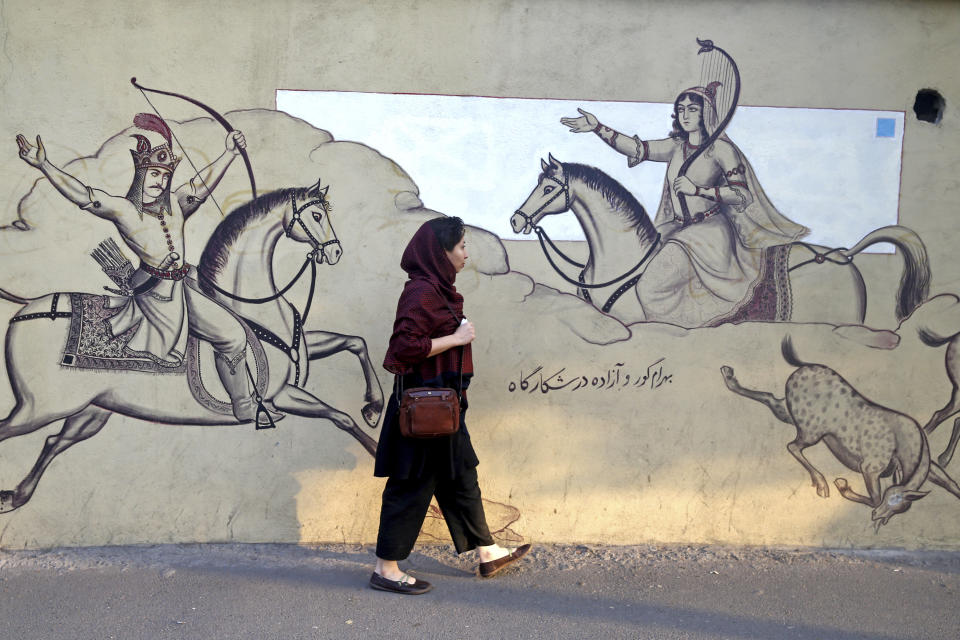 An Iranian woman walks past paintings of a Persian poetry in downtown Tehran, Iran, Monday, July 30, 2018. Iran's currency has dropped to a record low ahead of the imposition of renewed American sanctions, with many fearing prolonged economic suffering or possible civil unrest. (AP Photo/Ebrahim Noroozi)