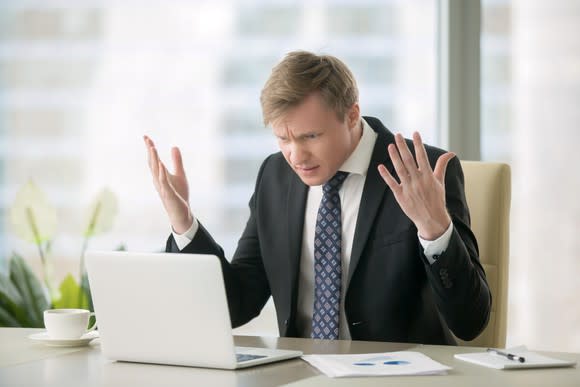 Puzzled businessman holding up hands while looking at laptop computer