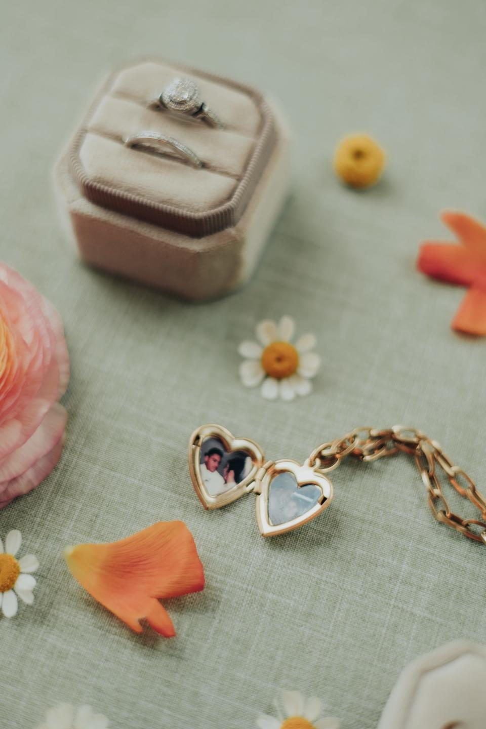 A ring box and a locket sit on a table with flowers.