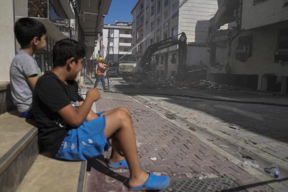 Two boys sit on a side and watch an excavator demolishing an old apartment building in Istanbul, Turkey, Friday, Aug. 4, 2023. Six months ago today, a devastating 7.8-magnitude earthquake hit the Kahramanmaras and 10 other provinces in southern Turkey on the morning of February 6th. Over 50,000 people died, and hundreds of thousands were left homeless, sheltering in tents and other temporary accommodation. (AP Photo/Khalil Hamra)