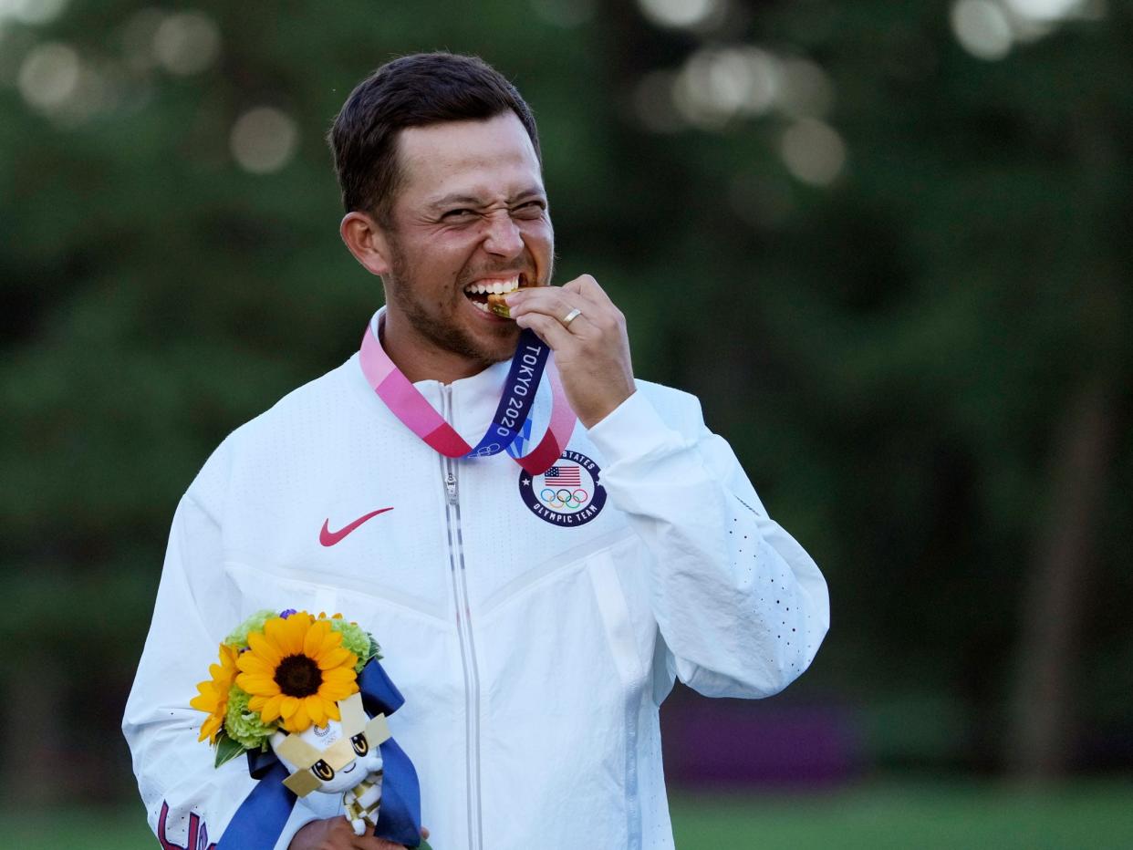 Xander Schauffele bites into his gold medal at Tokyo 2020.