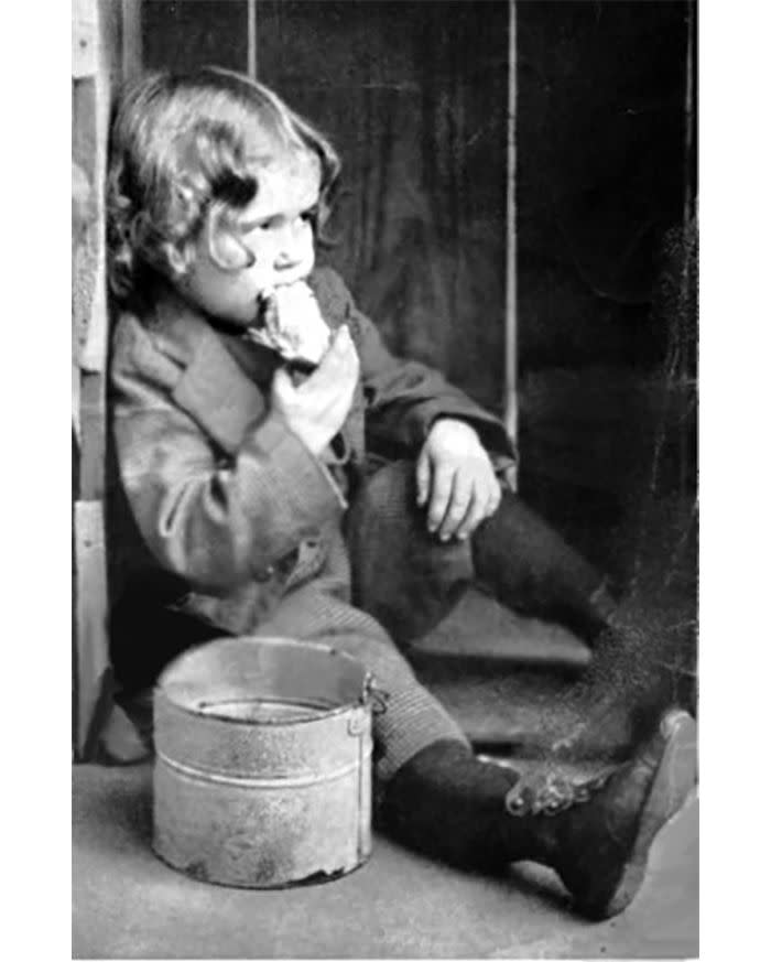 Young boy eating chicken out of a pail in the 1900s