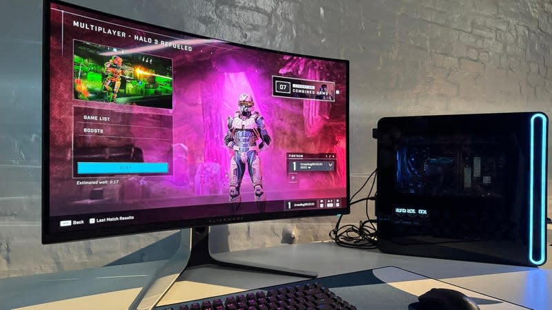 Alienware QD-OLED on a table next to a gaming PC.