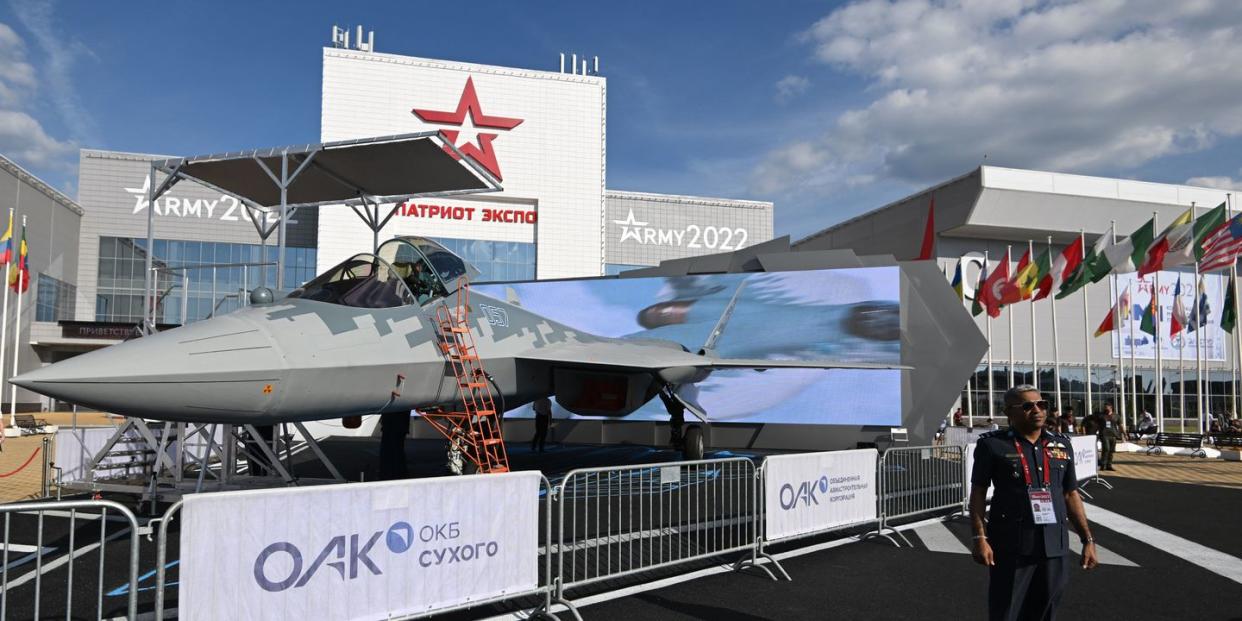 a foreign military official stands in front of a russian jet on display at the army 2022 expo