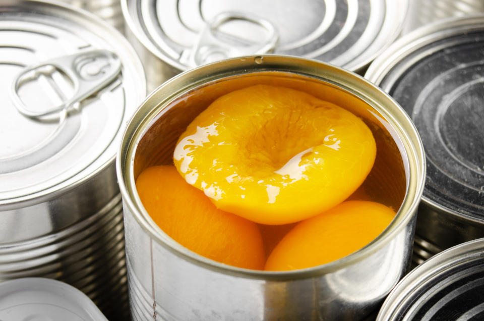 Canned peaches in syrup, open can among sealed ones