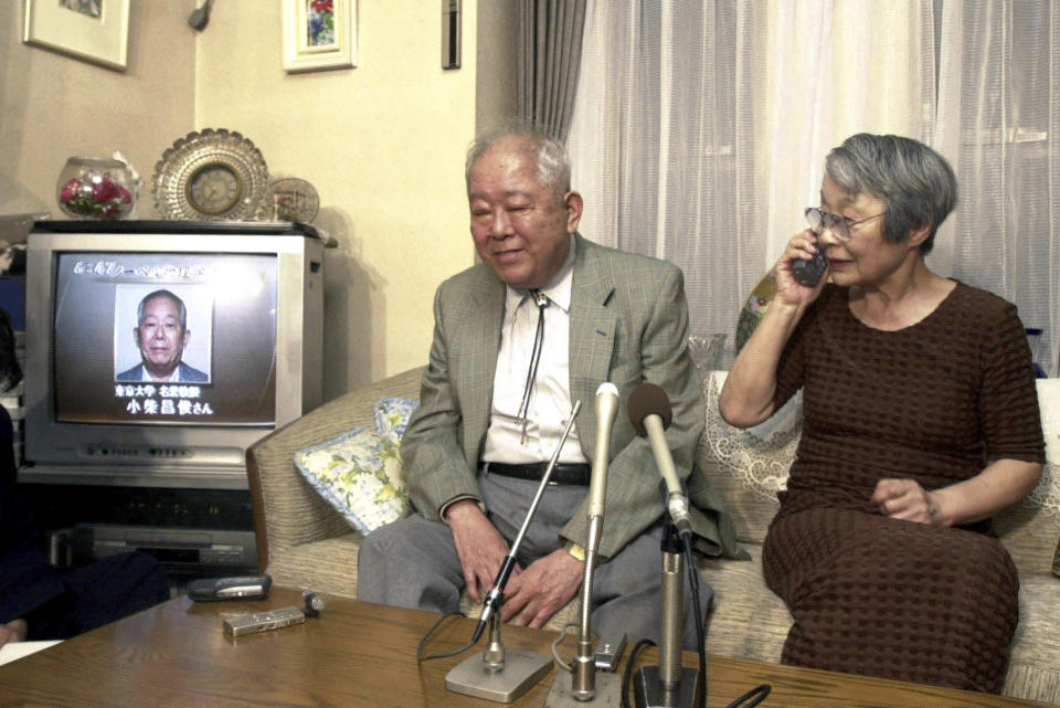 FILE - In this Oct. 8, 2002, Japanese physicist Masatoshi Koshiba sits with his wife Keiko Koshiba answering a congratulatory phone call as TV news reports his winning of the 2002 Nobel Prize in Physics at his home in Tokyo. Koshiba, a co-winner of the Nobel Prize for his pioneering researches into the make-up of the universe, died Thursday, Nov. 12, 2020, the University of Tokyo said. He was 94. (Kyodo News via AP, File)