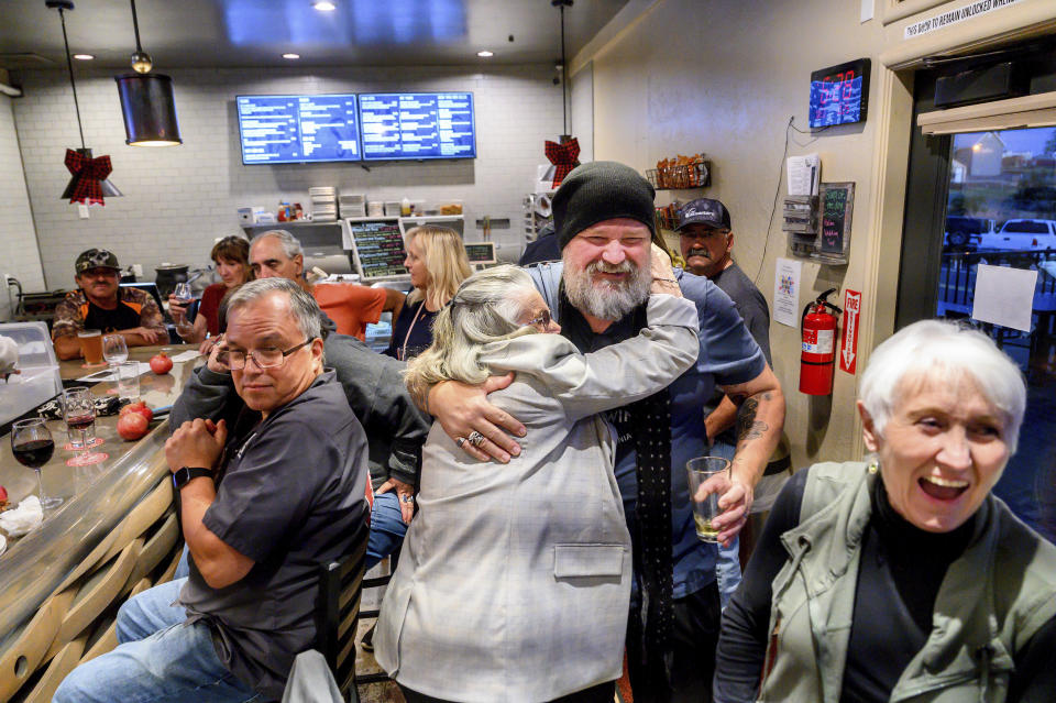 Jason Pieper hugs Kathy Desert at Nic's Deli & Wine Bar, Wednesday, Oct. 25, 2023, in Paradise, Calif. Pieper is in the process of opening the town's first brewery. Nic's owner, Nikki Jones, at right, lost two businesses in 2018's Camp Fire. (AP Photo/Noah Berger)