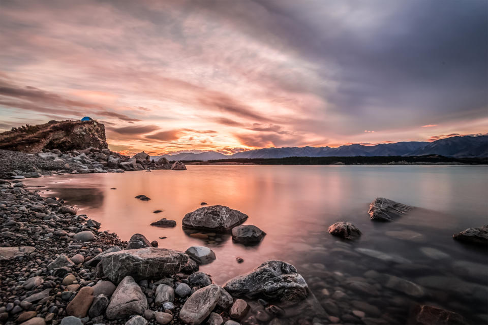 Sunset at Mount Cook National Park alongside Lake Pukaki with snow capped Southern Alps basking in the late winter afternoon's golden light. The setting sun cast vivid pastel  hues on the sky.