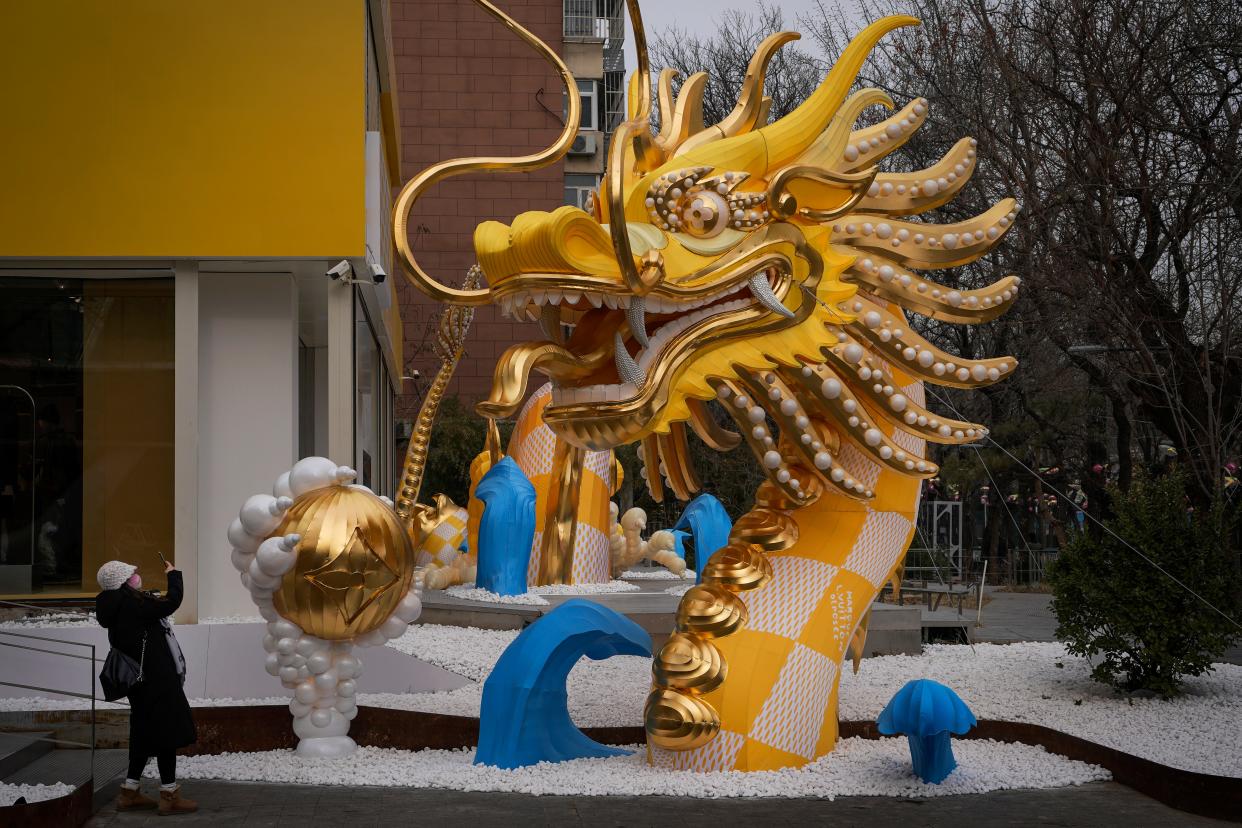 A woman takes a smartphone photo of a dragon figure on display outside a luxury fashion retail store in Beijing, Tuesday, Jan. 2, 2024. 2024 is the Year of the Dragon on the Chinese calendar. (AP Photo/Andy Wong)