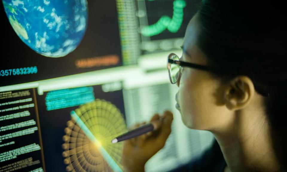 Young Asian woman, pointing at, and learning from, global data displayed on a large computer monitor.