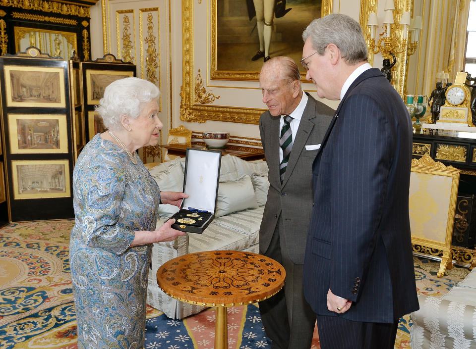 Queen Elizabeth II talks with the Australian High Commissioner Alexander Downer (R) as she prepares to present the Prince Philip, Duke of Edinburgh with the Insignia of a Knight of the Order of Australia, in the white drawing room at Windsor Castle on April 22, 2015 in Windsor, England.