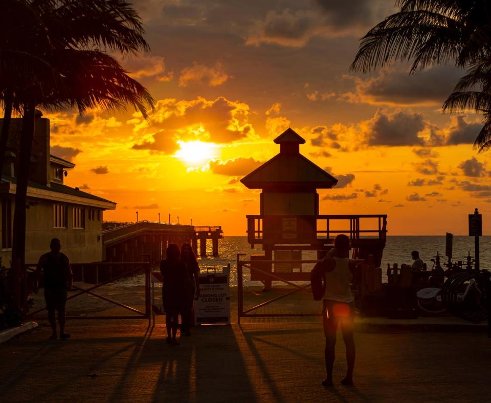 Un grupo de personas toma fotos del amanecer en el muelle de Sunny Isles mientras la pandemia del coronavirus continúa, el domingo 5 de abril de 2020, en Sunny Isles Beach.