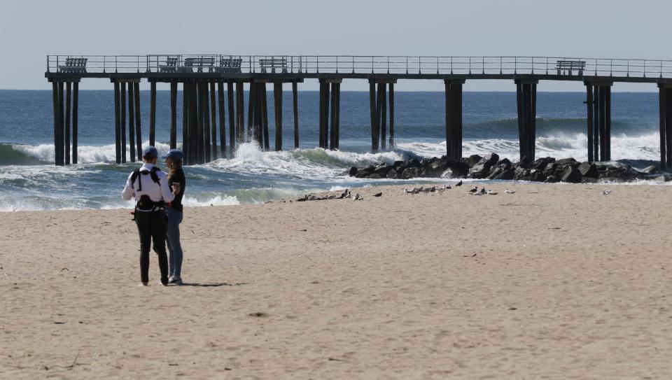 People stand on the beach near Ocean Grove's cross-shaped pier Monday, April 10, 2023. as work continues to finish the project.  The pier is scheduled to open to the public on April 15.  