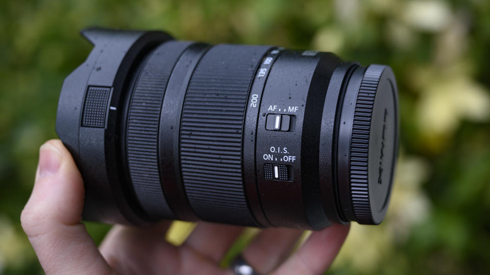 Panasonic Lumix S 28-200mm travel lens in the hand with leafy background and light rain