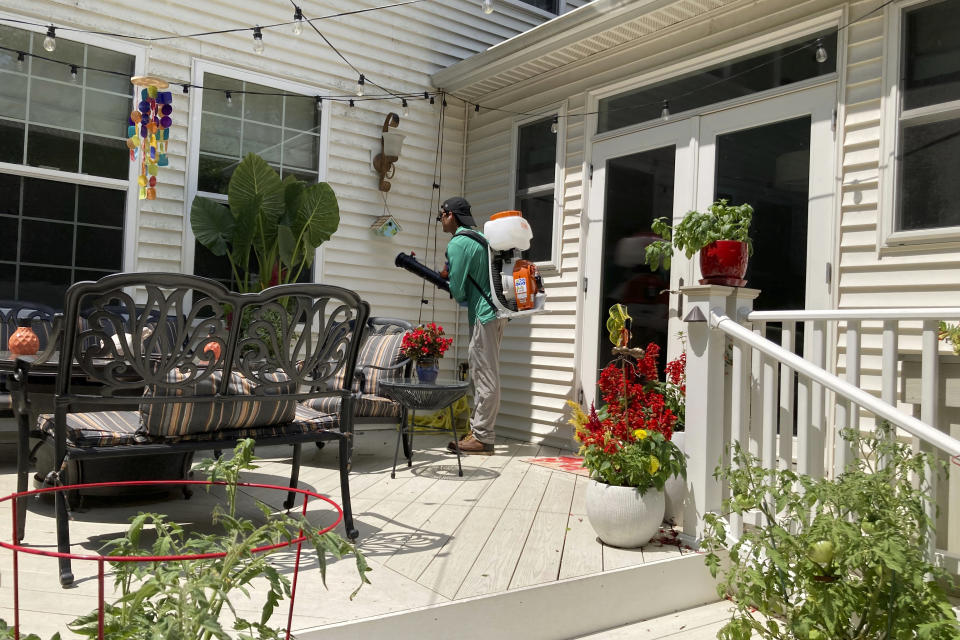 Mosquito Joe lead technician Damien Ysasi sprays a mixture of essential oil pesticides on a house in Cascade Township near Grand Rapids, Mich., on July 20, 2022. As climate change widens the insect's range and lengthens its prime season, more Americans are resorting to the booming industry of professional extermination. But the chemical bombardment worries scientists who fear over-use of pesticides is harming pollinators and worsening a growing threat to birds that eat insects. (AP Photo/John Flesher)