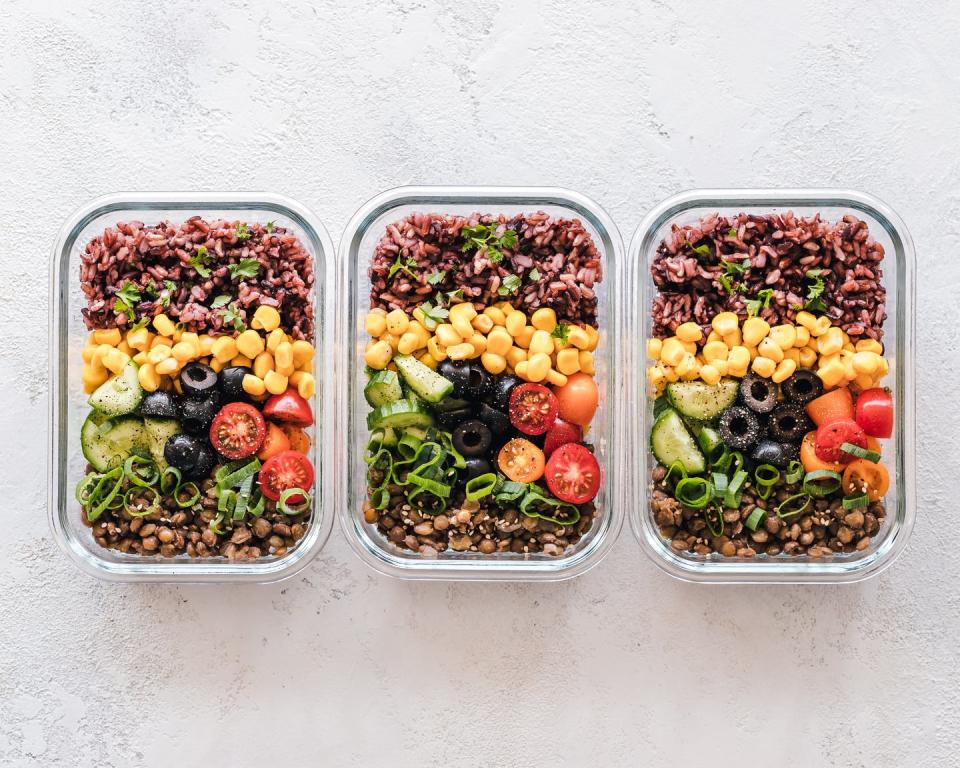 Plant based meal prep, three tupperware containers are shown with rice, corn, avocado, tomato, beans and olives