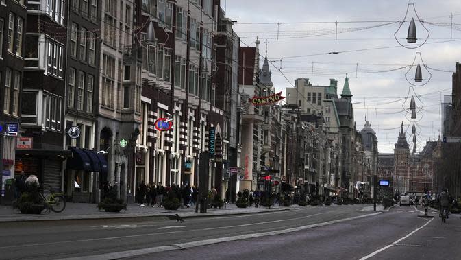 Orang-orang melewati toko-toko yang tutup di jalan perbelanjaan yang biasa ramai di pusat kota Amsterdam, 20 Desember 2021. Negara-negara di Eropa mempertimbangkan pembatasan yang lebih ketat guna membendung gelombang baru infeksi COVID-19 yang didorong oleh varian omicron.  (AP Photo/Peter Dejong)