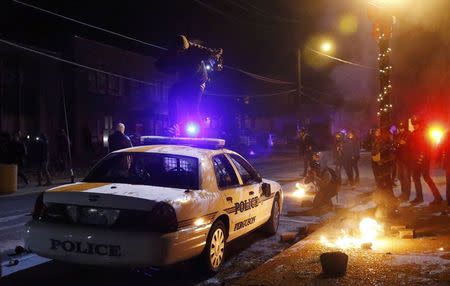 A protester jumps on a Ferguson police car set on fire by protesters in Ferguson, Missouri, November 25, 2014. REUTERS/Jim Young