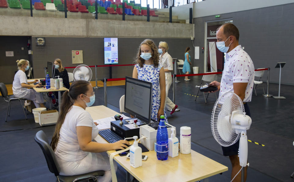Gloria Raudjarv, 13-year-old girl, center, and her father Ivo, right, stand in front of a nurse to be registrateto for her first dose of the Covid-19 vaccine a vaccination center inside a sports hall in Estonia's second largest city, Tartu, 164 km. south-east from Tallinn, Estonia, Thursday, July 29, 2021. Estonia's second largest city Tartu is making rapid progress in vaccinating children aged 12-17 ahead of the school year in September. Around half of the town's teenagers have already received their first vaccine, and local health officials are confident they will hit 70% in the coming 30 days. (AP Photo/Raul Mee)