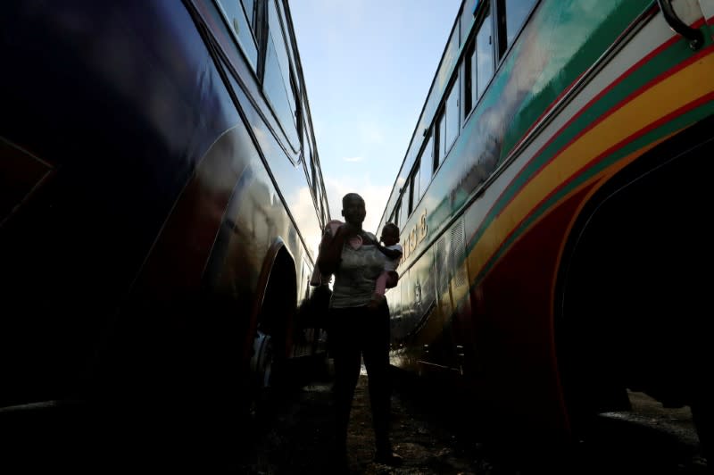 A passenger carries her child before boarding a disinfected public transport bus as residents leave for the villages amid concerns over the spread of coronavirus disease (COVID-19) in Nairobi