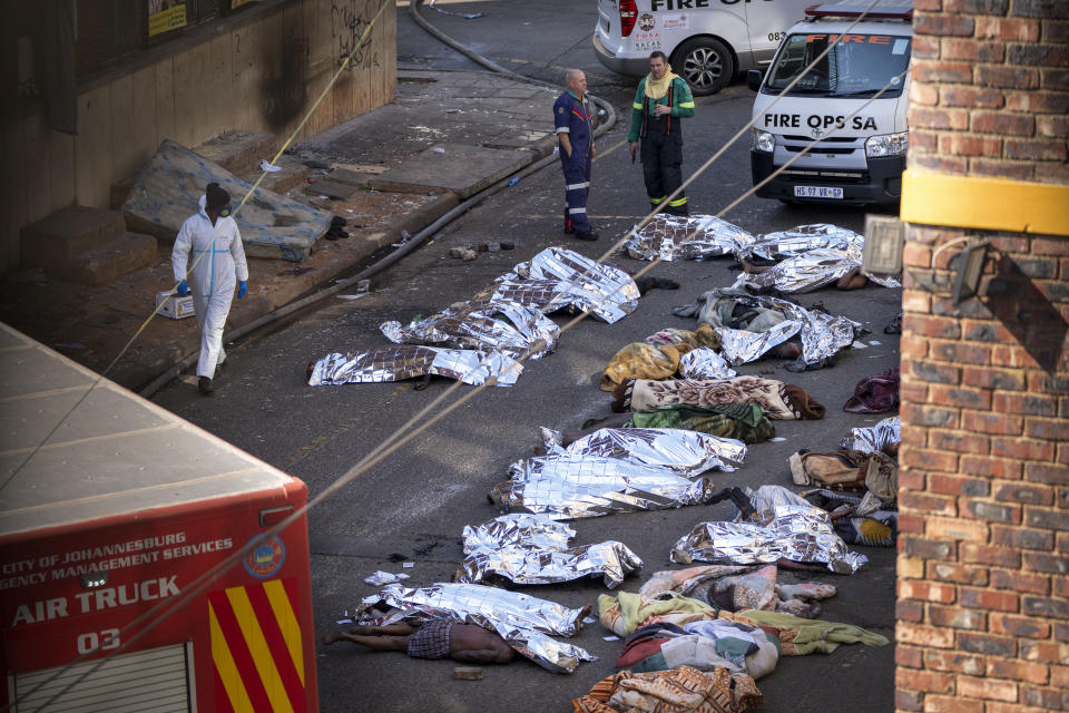 Varios médicos, junto a los cadáveres cubiertos de las víctimas de un incendio en un edificio del centro de Johannesburgo, el 31 de agosto de 2023. (AP Foto/Jerome Delay)