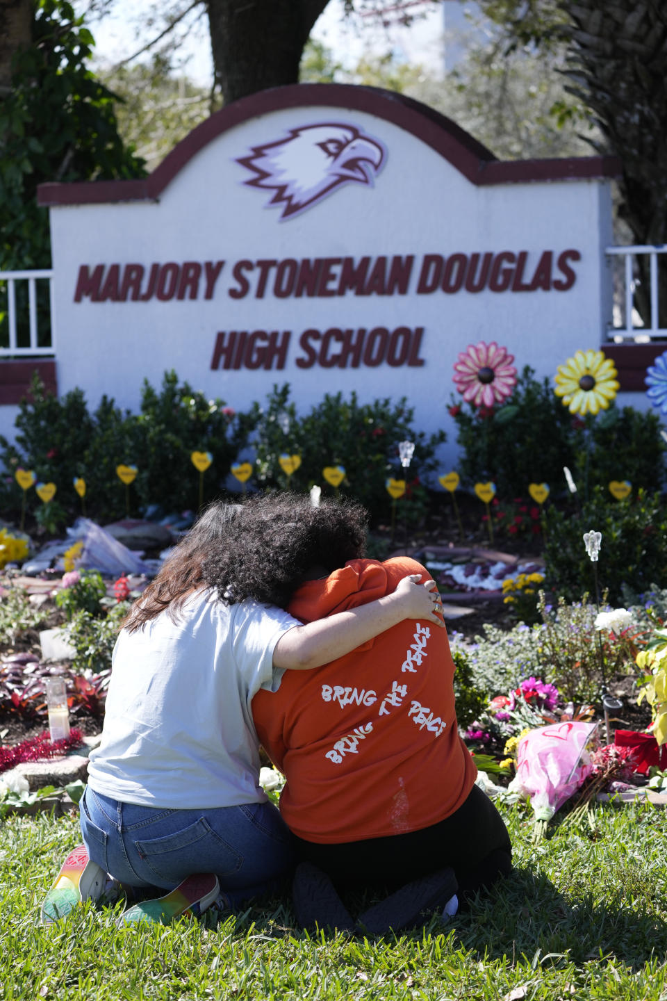 FILE - Mourners take a moment, Tuesday, Feb. 14, 2023, in front of a memorial at Marjory Stoneman Douglas High School in Parkland, Fla. A reenactment of the 2018 massacre that left 17 dead, 17 wounded and hundreds emotionally traumatized, is scheduled to be conducted Friday, Aug. 4, 2023, as part of lawsuits filed by the victims' families and the injured. (AP Photo/Wilfredo Lee, File)