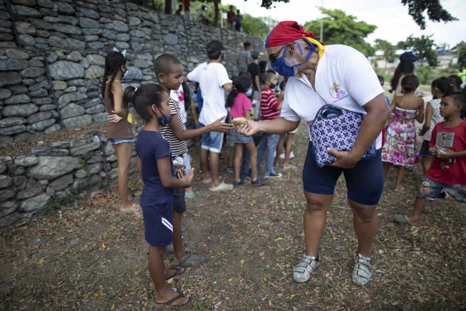 Andres Burgos, a 55-year-old publicist, hands a package of homemade arepas or corn flour patties to a child in Macuto, Venezuela, Saturday Oct. 24, 2020. Burgos rode to the seaside city in Venezuela's La Guaira state, accompanied by other cyclists to distribute the arepas to needy children, adults and the elderly. (AP Photo/Ariana Cubillos)