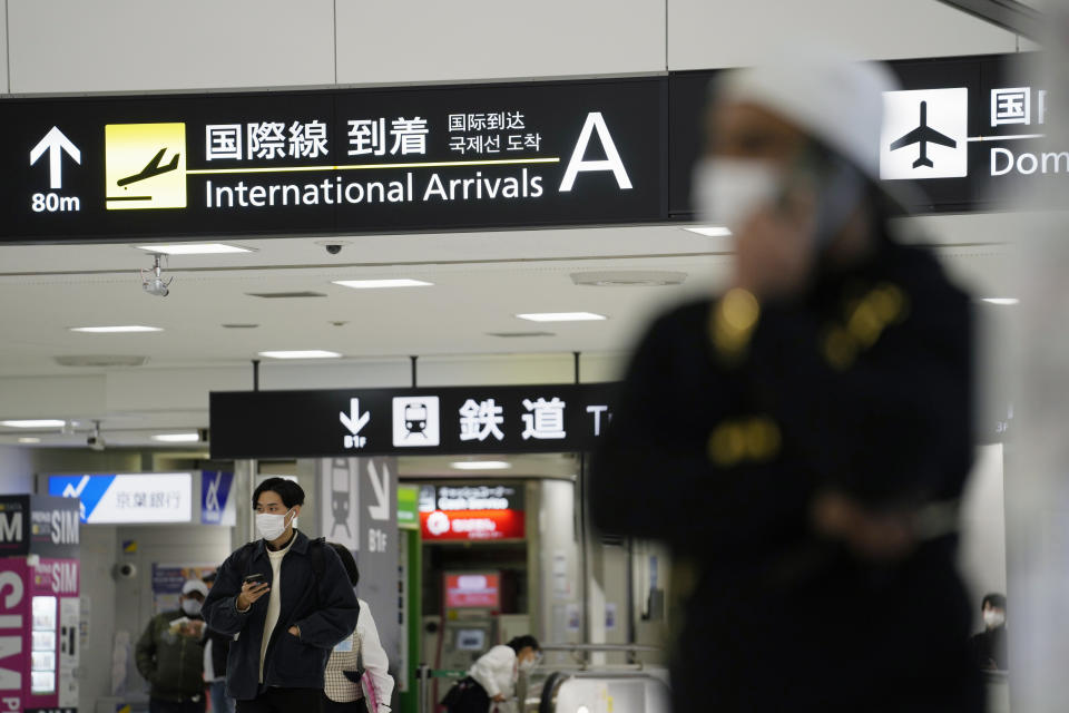 Men hold their phones as they stand by an arrival gate for international flights at the Narita International Airport in Narita, east of Tokyo, Thursday, Dec. 2, 2021. Going further than many other countries in trying to contain the virus, Japan has banned foreign visitors and asked international airlines to stop taking new reservations for all flights arriving in the country until the end of December.(AP Photo/Hiro Komae)