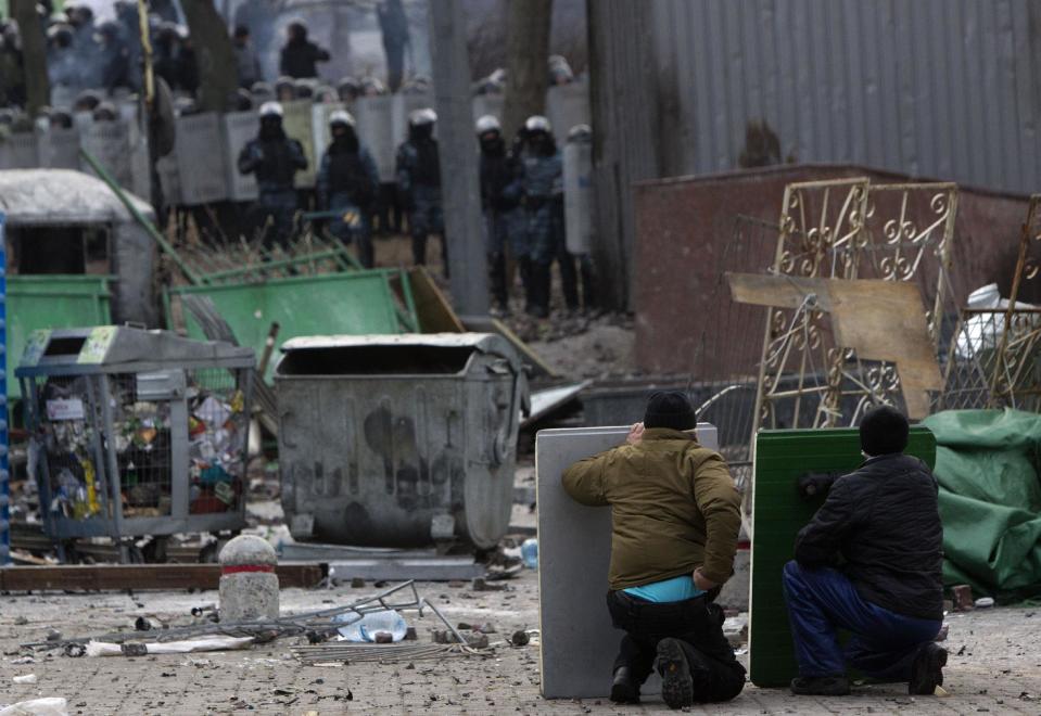 Protesters shield themselves, during clashes with police in central Kiev, Ukraine, Monday, Jan. 20, 2014. Protesters erected barricades from charred vehicles in central Kiev as the sound of stun grenades pierced the freezing air, after a night of rioting sparked by passage of laws aims at curbing street protests. (AP Photo/Sergei Chuzavkov)