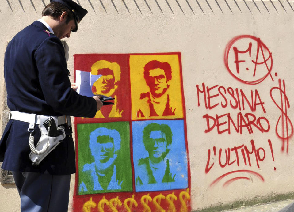 FILE - An Italian Police officer looks on at graffiti on the perimeter wall of Palermo's city's cathedral, portraying Matteo Messina Denaro, a fugitive Mafia boss, in Sicily, southern Italy, Thursday, April 24, 2008. Matteo Messina Denaro, a convicted mastermind of some of the Sicilian Mafia’s most heinous slayings, died on Monday, Sept. 25, 2023, in a hospital prison ward, several months after being captured as Italy’s No. 1 fugitive and following decades on the run, Italian state radio said. Writing at right of the dollar sign, says: "Messina Denaro The Last One!" (AP Photo/Alessandro Fucarini, File)