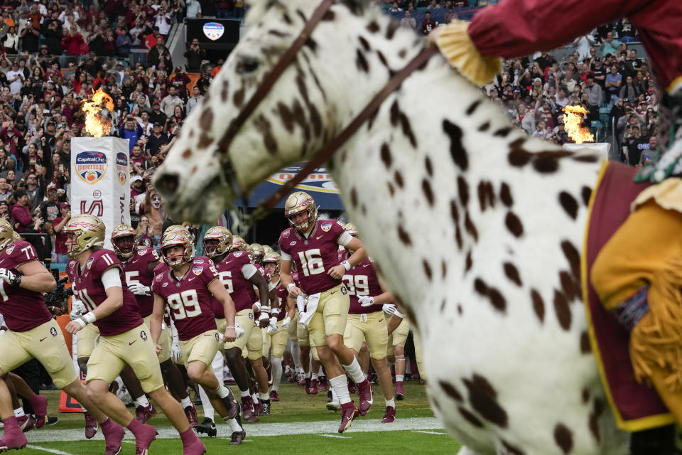 Florida State players run onto the field as the their mascot Chief Osceola rides past on Renegade, at the start of the Orange Bowl NCAA college football game against Georgia, Saturday, Dec. 30, 2023, in Miami Gardens, Fla. (AP Photo/Rebecca Blackwell)