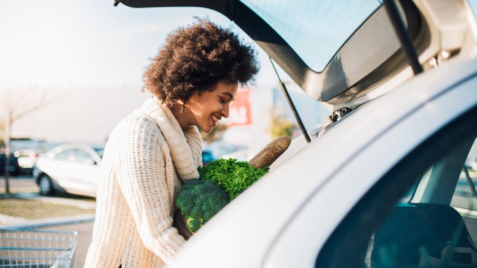 Young woman putting groceries at the car trunk.