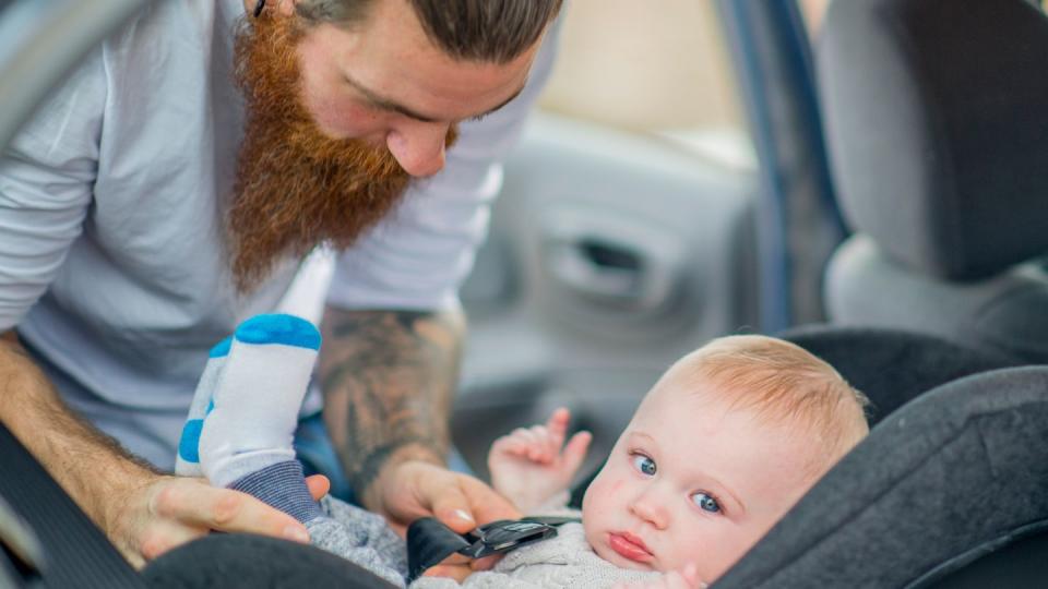 man buckling baby into car seat