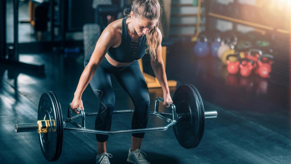 Woman performing a hex bar deadlift mid lift in a  gym